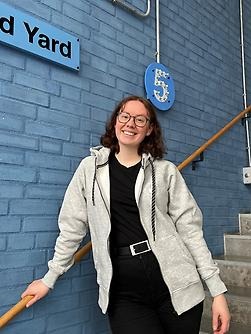 Girls stands on stairs with one hand on bannister, learning to her right and smiling.